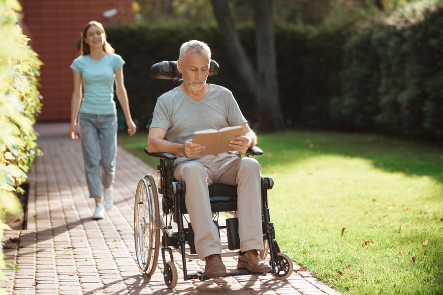 Man in wheelchair reading a book in garden